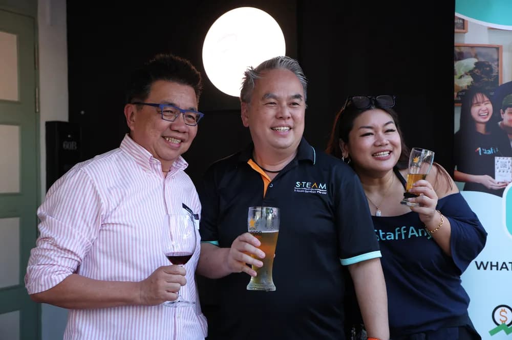Three attendees smiling together with drinks at a StaffAny Singapore community event